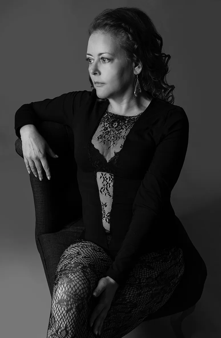 Frau in Spitzenbody sitzend auf Sessel zur Seite blickend