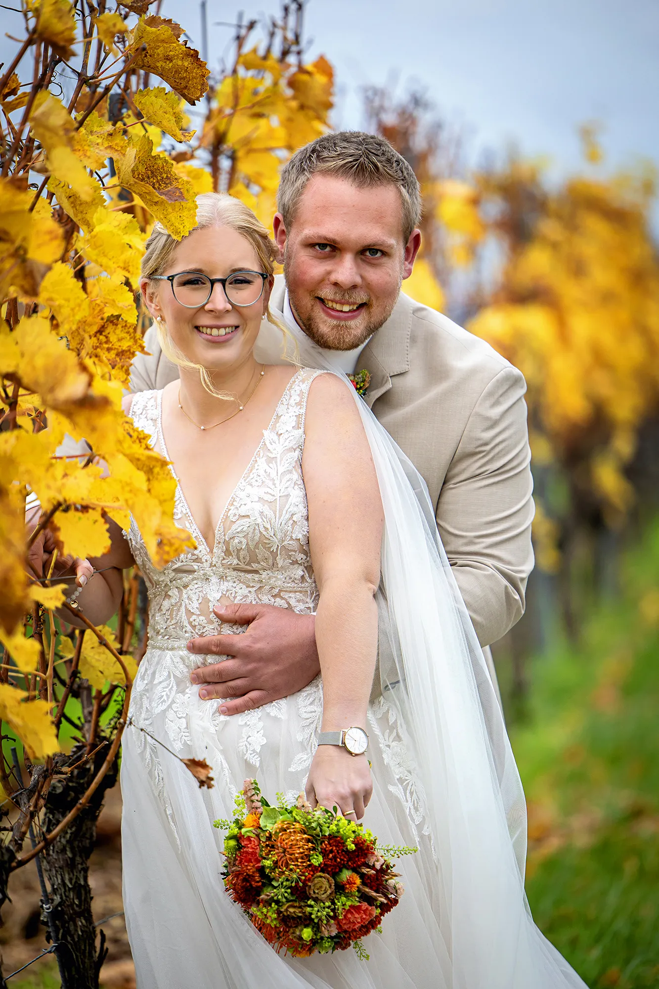 Bräutigam umarmt Braut von hinten vor gelbem Herbstlaub im Weinberg